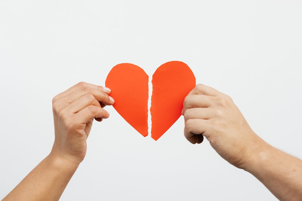Infertility Grief - A close-up view of hands holding a torn red paper heart, symbolizing heartbreak or relationship issues.