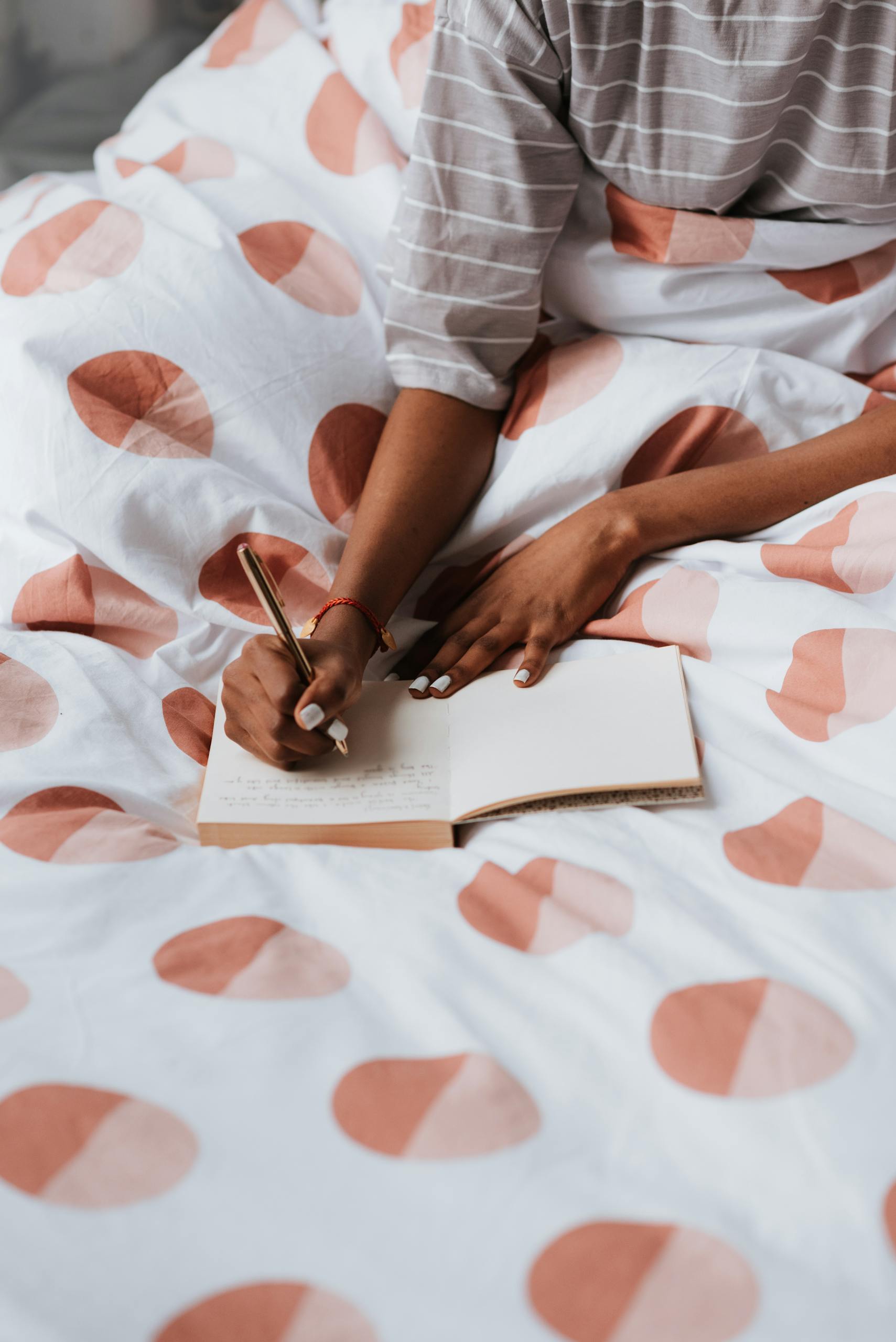 Person writing in a notebook on a patterned bedspread. Relaxed and creative atmosphere.